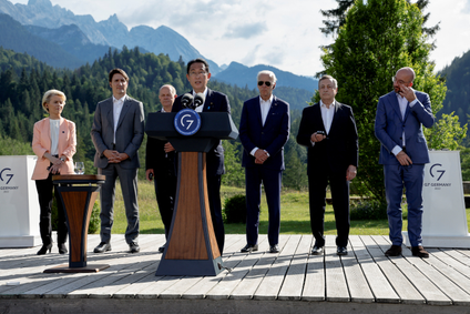 G7 leaders are shown standing on a stage with mountains in the background.