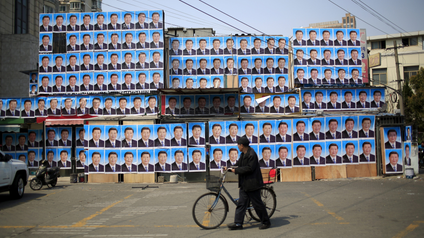 Man with bicycle walks by Xi Jinping posters