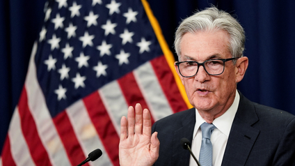 U.S. Federal Reserve Board Chairman Jerome Powell raises his hand before the podium at a press conference.