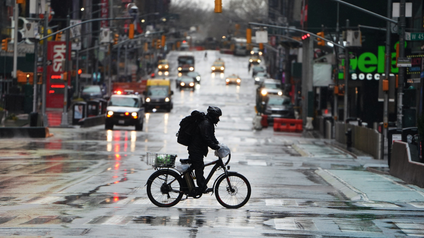A delivery person on an electric bike rides across a mostly-empty wet street in New York at the start of the pandemic..