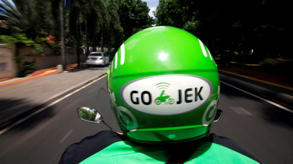 The back of a green helmet is show on a person that is riding a scooter.