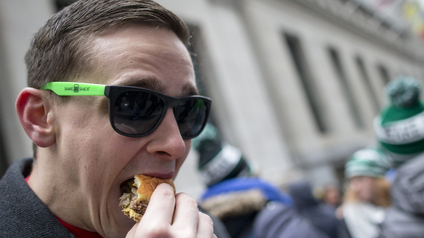 A man eats a Shake Shack burger in front of New York Stock Exchange