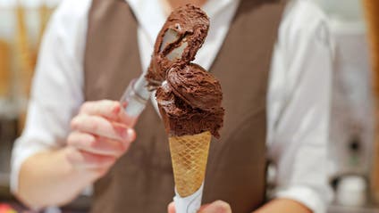 An ice-cream shop worker scoops a cone of chocolate ice cream