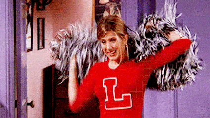 Jennifer Aniston waves pom-poms in a red cheerleading uniform.
