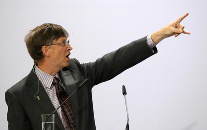 Bill Gates is pictured in front of a microphone and he's pointing at something with his mouth open.