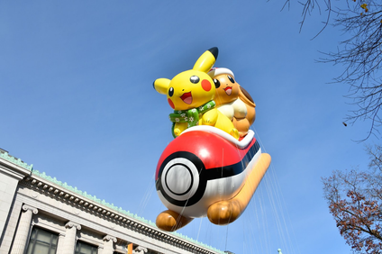 Two Pokemon characters riding a Pokemon-themed sleigh and wearing scarves, only they are also a giant balloon flying over a city building.