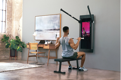 A weight lifter works out at home in front of a screen.