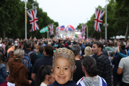 A man wearing a mask depicting Queen Elizabeth II stands along The Mall during the Platinum Party At The Palace concert outside Buckingham Palace on June 4, 2022 in London, United Kingdom. The Platinum Jubilee of Elizabeth II is being celebrated from June 2 to June 5, 2022, in the UK and Commonwealth to mark the 70th anniversary of the accession of Queen Elizabeth II on 6 February 1952.