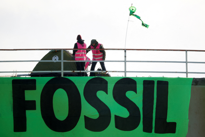 Two people in pink vests stand near a tent on top of a storage tank. They hung up a sign that reads fossil.
