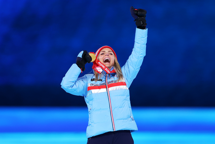 Gold medalist Therese Johaug, wearing a blue jacket with a red stripe and black gloves, holds her gold medal in one hand, has her other fist in the air and applauds victoriously during the ceremony of Women's 30km Mass Start medal presentation during the Beijing 2022 Winter Olympics Closing Ceremony on Day 16 of the Beijing 2022 Winter Olympics.