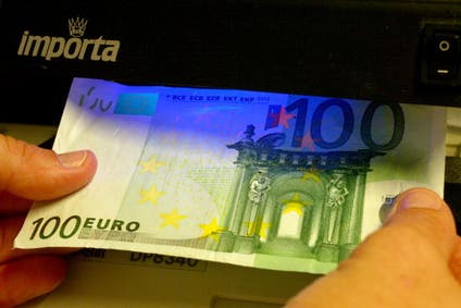 A shopkeeper holds a 100 Euro note against ultra-violet light to check if it is real