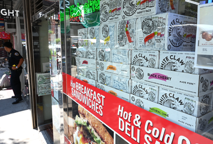 A window of a convenience store shows boxes of White Claw seltzers. 