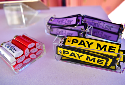 Key chains that say "pay me" and "self-love" are shown next to lighters that say "girlboss"