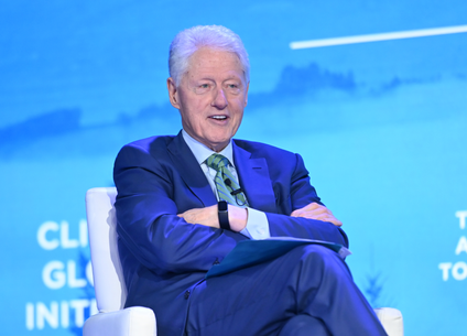 Former US president Bill Clinton sits with his arms folded. 