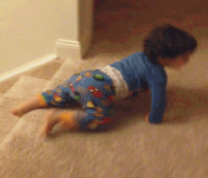 A gif of a happy child sliding on its stomach down the stairs, in pajamas.