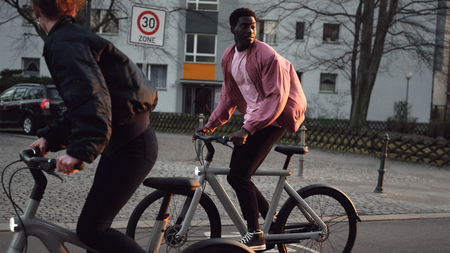 Um homem de camisa rosa anda de bicicleta elétrica Van Moof