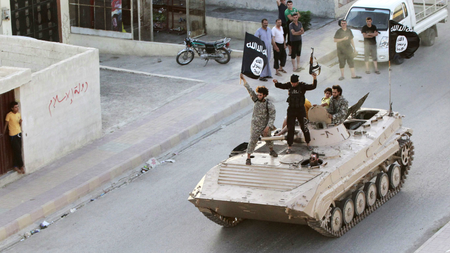 Militant Islamist fighters hold the flag of Islamic State (IS) while taking part in a military parade along the streets of northern Raqqa province in this June 30, 2014 file photo