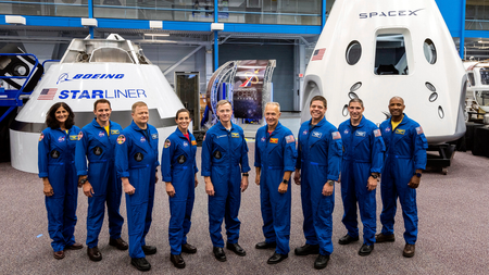This undated photo made available by NASA on Friday, Aug. 3, 2018 shows, from left, Sunita Williams, Josh Cassada, Eric Boe, Nicole Mann, Christopher Ferguson, Douglas Hurley, Robert Behnken, Michael Hopkins and Victor Glover standing in front of Boeing’s CST-100 Starliner and SpaceX’s Crew Dragon capsules at the Kennedy Space Center in Florida. On Friday, the space agency announced the astronauts who will ride the first commercial capsules into orbit next year and bring human launches back to the U.S.
