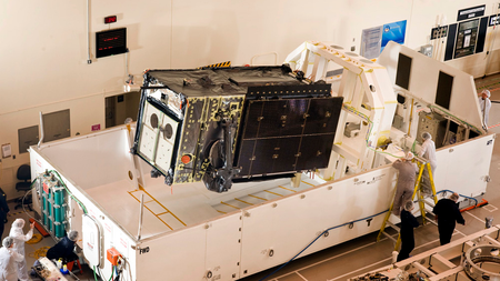 A satellite roughly the same size as Space Vehicle Four is loaded into a transport container.