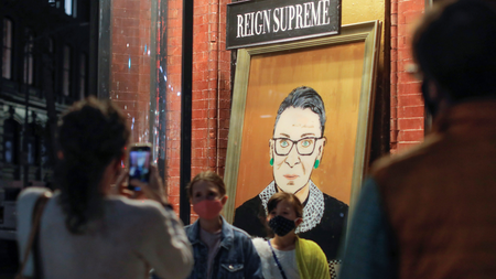 Children are photographed in front of a painting in a storefront on Broadway of Associate Justice of the Supreme Court of the United States Ruth Bader Ginsburg who passed away in Manhattan, New York City