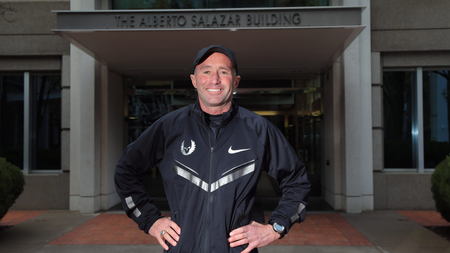 Alberto Salazar stands smiling with his hands on his hips.