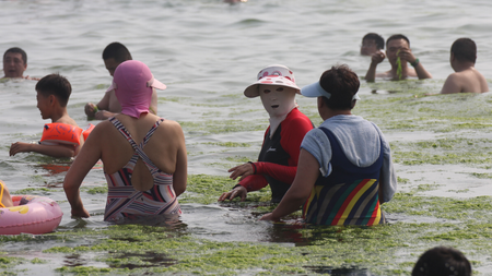 A masked female holidaymaker, center, talks with others at a beach resort on a scorching day in Qingdao city, east Chinas Shandong province, 3 July 2013. Holidaymakers are flooding to the beach resorts to cool down in the eastern Chinese coastal city of Qingdao as heat waves are sweeping through many parts of China. A group of female swimmers are spotlighted among the others as they dress their heads up with colorful masks, making them look like masked robbers or terrorists. Dubbed as the bikini for faces, the mask is used to protect the face of its user from being tanned by scorching sunlight and stung by jellyfish. Priced at 15-20 yuan (US$2.44-US$3.26) apiece, the mask is quite popular among middle-aged and elderly women.(Imaginechina via AP Images