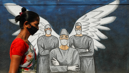 Woman wearing a protective mask walks past a graffiti amidst the spread of COVID-19, in Navi Mumbai