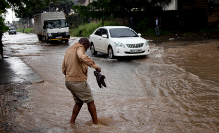 A man holds his shoes in his hand as he crosses a flooded street during heavy rain, in downtown Nairobi, Kenya.
