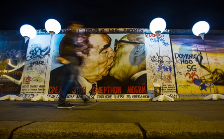 A person passes by the installation &#039;Lichtgrenze&#039; (Border of Light) in front of a painting depicting former Soviet leader Leonid Brezhnev kissing his East German counterpart Erich Honecker (R) along the East Side Gallery, the largest remaining part of the former Berlin Wall, in Berlin November 7, 2014. A part of the inner city of Berlin is being temporarily divided from November 7 to 9, with a light installation featuring 8000 luminous white balloons, following the 9.5-mile (15.3 kmilometre) path the Berlin Wall once occupied, to commemorate the 25th anniversary of the fall of the Wall. REUTERS/Hannibal Hanschke (GERMANY - Tags: ANNIVERSARY ENTERTAINMENT CITYSCAPE TPX IMAGES OF THE DAY) - RTR4DAPP