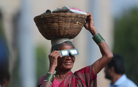 A roadside vender holding a basket on her head watches the eclipse in Hyderabad