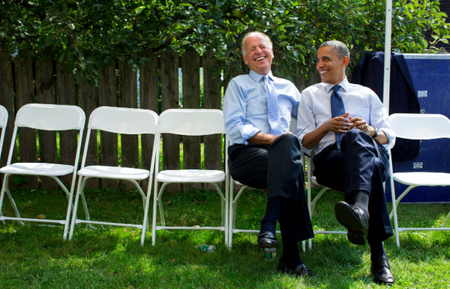 In New Hampshire, Sept. 7, 2012. President Obama sits on a white folding chair next to Vice President Biden joking with the Vice President Joe Biden before a campaign rally in Portsmouth. The two look at each other smiling.