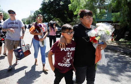 A woman and a childarrive to Robb Elementary school with flowers, the day after a gunman killed 19 children and two teachers at the school in Uvalde, Texas