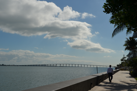 A man walks next to a sea wall, which rises above the calm, blue expanse of Biscayne Bay.