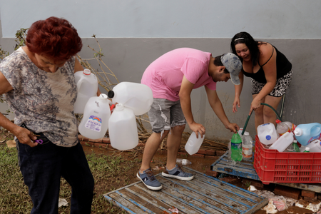 Residents use a water faucet on the side of a building to fill water jugs due to lack of water service following Hurricane Maria