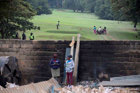 A golfer tees in the background as Kenyans watch bulldozers demolishing dozens of houses to make way for a new road in the Kibera slum in Nairobi, Kenya, July 23, 2018.