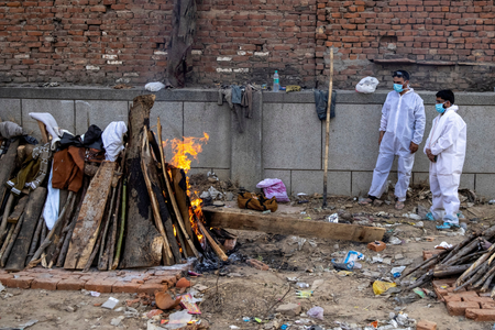 Relatives stand next to the burning funeral pyre of a person, who died due to the coronavirus disease (COVID-19), at a crematorium ground in New Delhi