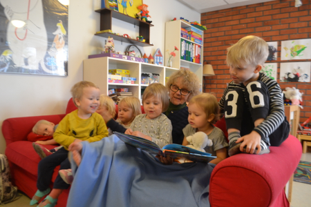 A group of children sit on the couch with Marjatta as she reads them a book