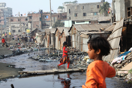 A girl walks across polluted water in a slum in Dhaka, Bangladesh