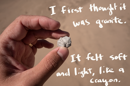 An image of a hand holding a gray piece of what looks like a rock. There&#039;s handwriting on top of the photo that says: &quot;I first thought it was granite. It felt soft and light, like a crayon.&quot;