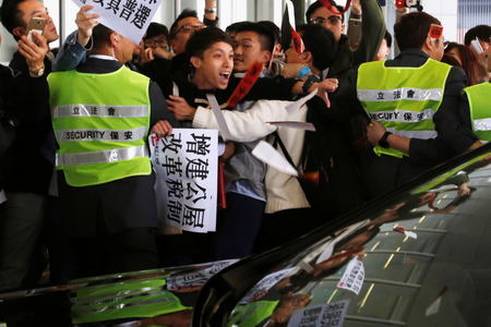 A crowd of protesters, one carrying a placard reading &quot;build more public housing, reform tax system&quot;, is pushed back by security workers in Hong Kong, China in 2018.