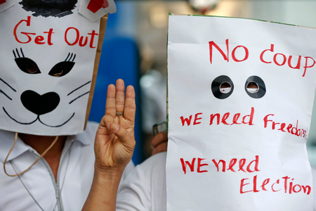 Anti-coup protesters wear paper bags with messages written on them as they flash a three-finger sign during a protest at a shopping mall in Bangkok