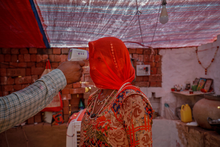 A healthcare worker checks the temperature of a woman inside her hut during a coronavirus disease vaccination drive for workers at a brick kiln in Kavitha village on the outskirts of Ahmedabad in April 2021.