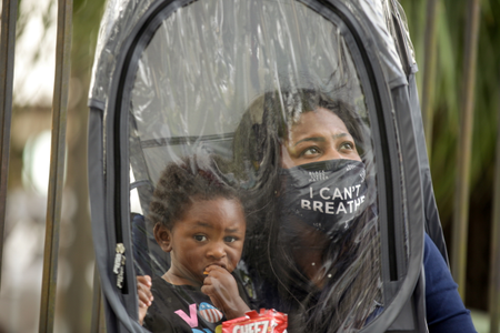 Dana Clarke, wearing an &quot;I can&#039;t breathe&quot; mask, holds her son inside a clear protective suit as she waits to vote early.