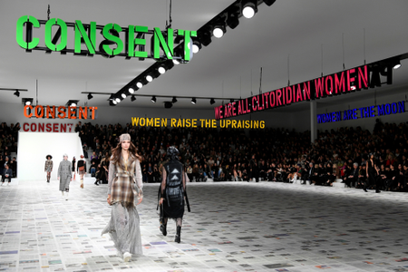 Models walk under signs that read &quot;consent&quot; and &quot;women raise the upraising&quot; at the Dior fall-winter 2021 show