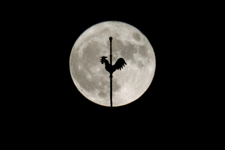 The rising supermoon is seen behind the weathercock of the church of Saint-Hilaire in the village of Saint-Fiacre-sur-Maine near Nantes, western France November 14, 2016.