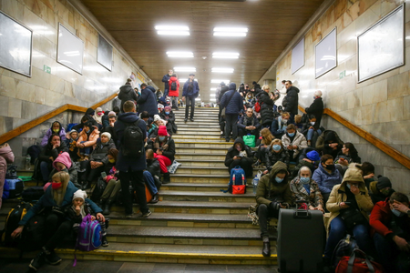 Many people sit on either side of a stairwell in a fluorescent-lit subway station in Ukraine.