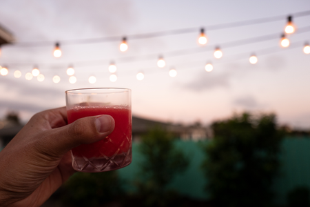 A photo of a hand holding up a glass of the finished cocktail: frosé. The scene is a backyard at sunset.