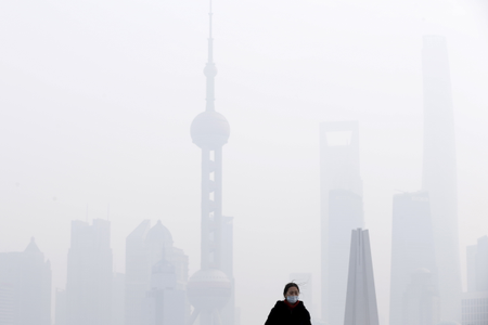 A woman wearing a face mask stands on a bridge in front of the financial district of Pudong amid heavy smog in Shanghai, China, December 15, 2015.
