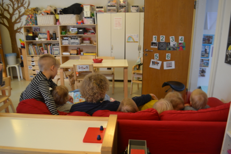 A view of Marjatta on the couch reading to a group of children from the back