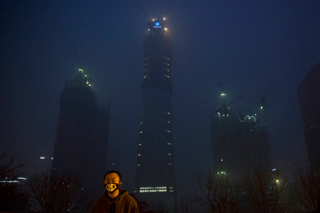 A man wears a mask with a skeleton design near the smoggy night scene of the Central Business District under construction in Beijing, China on Dec.21, 2016. Chinese weather forecasters and state media say the dense, gray smog that has smothered much of China, closing schools and grounding planes, may finally soon give way. (AP Photo/Ng Han Guan)